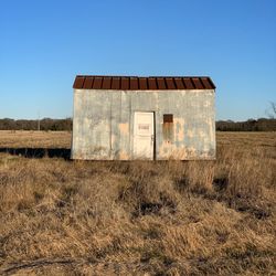 Abandoned built structure on field against clear blue sky