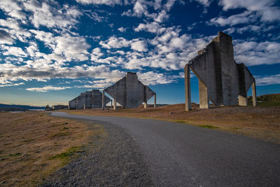 Road passing through field against cloudy sky