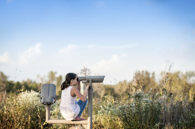 Teen girl looking out at nature through a telescope