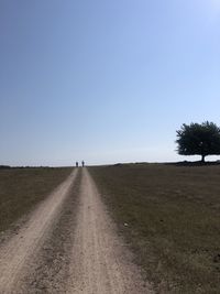 Dirt road amidst field against clear sky