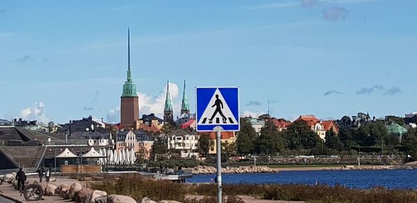 Road sign by buildings against sky in city