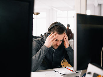 Tensed executive wearing headphones at desk in office