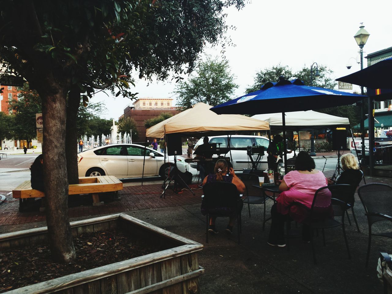 tree, chair, lifestyles, leisure activity, men, building exterior, bench, person, table, built structure, restaurant, relaxation, sitting, architecture, sunlight, sidewalk cafe, city, cafe, outdoors