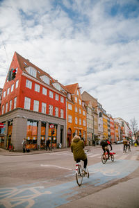 People riding bicycle on street against buildings in city