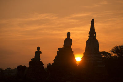 Low angle view of silhouette buddha statues against sky during sunset