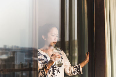 Portrait of young woman looking through window