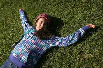 High angle view of smiling girl resting on grassy field with eyes closed