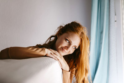 Smiling young woman with hand on chin looking down at home