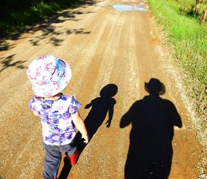 High angle view of girl walking on dirt road during sunny day