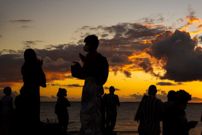 Silhouette people on beach against sky during sunset