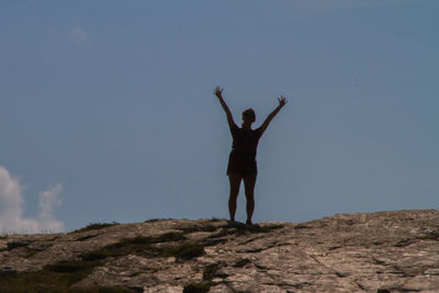 Rear view of woman standing on rock against sky