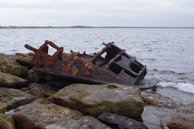 Abandoned boat on sea shore against sky