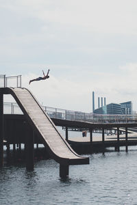 Silhouette man jumping by pier in sea