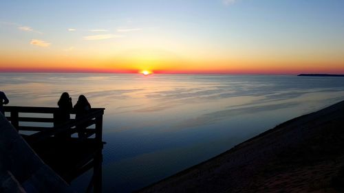 Silhouette women standing on pier at beach against sky during sunset