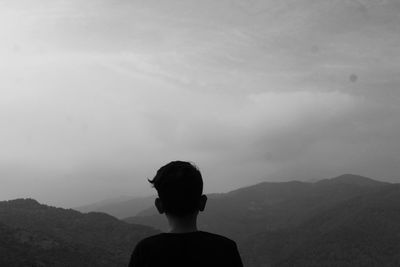 Rear view of man looking at mountains against sky