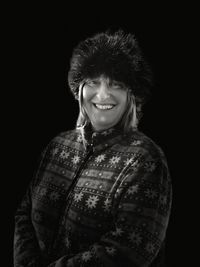 Portrait of mature woman smiling while wearing fur hat against black background