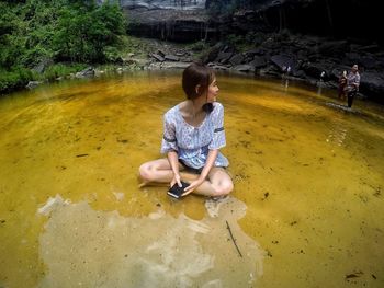 Fish-eye view of woman sitting with mobile phone in river