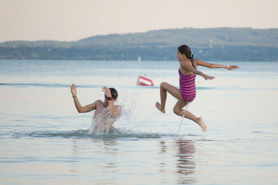 Teenage siblings enjoying in sea during sunset