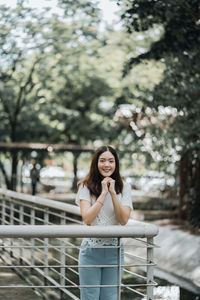 Portrait of smiling young woman standing against railing