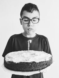 Boy blowing lit candle on cake against white background