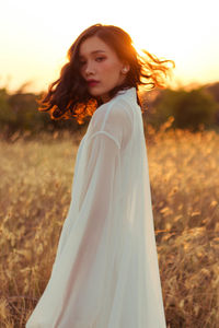 Young woman standing on field against sky during sunset