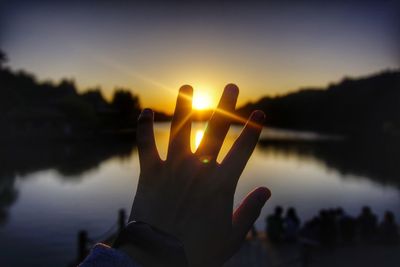 Close-up of hand against lake during sunset