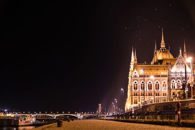 Hungarian parliament building by road against sky in city at night