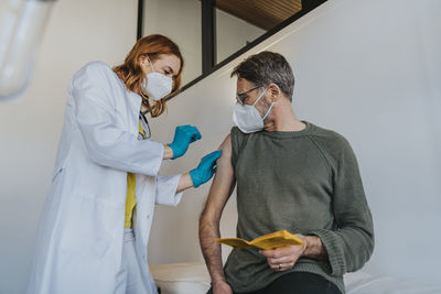 Female expertise injecting covid-19 vaccine dose in patient arm while standing at examination room