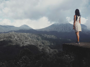 Rear view of woman standing on observation point against mountains and sky