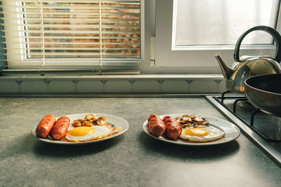 Breakfast set of sausages fried eggs and mushroom on the kitchen counter by the window.