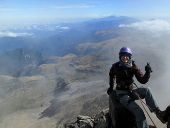 Happy woman sitting on rock at mountain in foggy weather