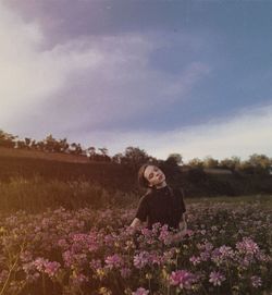 Woman with purple flowers on field against sky