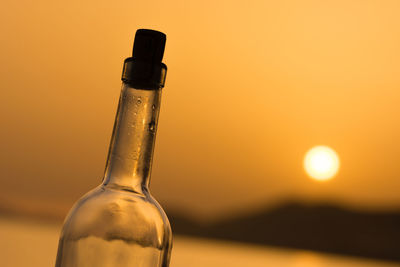 Close-up of bottle at beach against sky during sunset