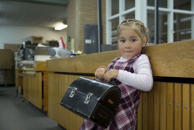 Portrait of cute girl with metallic suitcase standing in office 