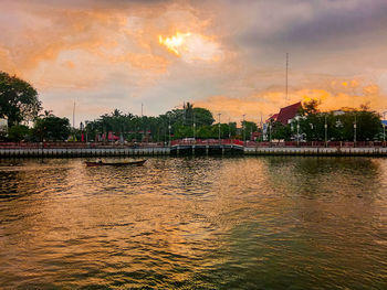 Scenic view of river by buildings against sky at sunset