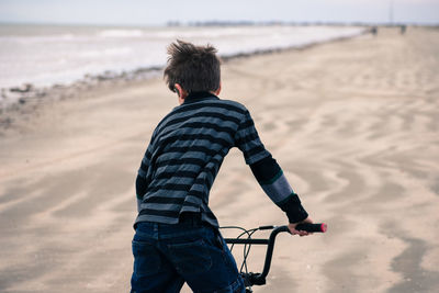 Rear view of boy cycling at beach