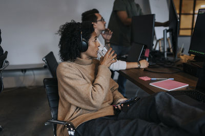 Businesswoman drinking coffee while looking at computer hacker working in startup company