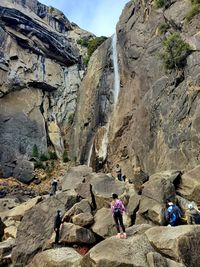 Rear view of people climbing on rocks below a waterfall