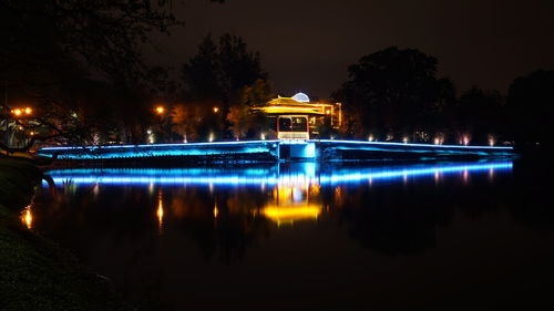 Illuminated building by lake against sky in city at night