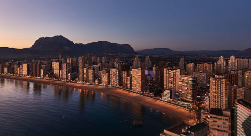 Panoramic view of silhouette cityscape by mountains against sky during sunset