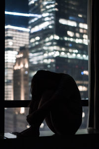 Silhouette woman sitting against window at night
