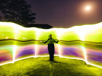 Rear view of man standing against illuminated rainbow in sky