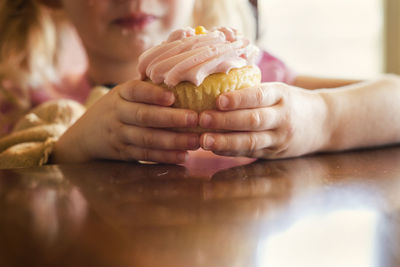 Midsection of girl holding cupcake at table in house