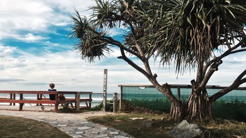 Woman sitting on bench by sea against cloudy sky