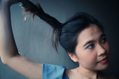 Close-up of young woman holding hair against wall