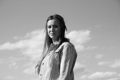 Low angle portrait of smiling young woman standing against sky