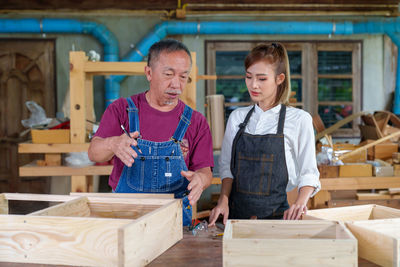 Tutor with female carpentry student in workshop studying for apprenticeship at college ,