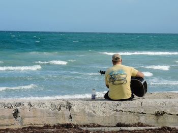 Rear view of man sitting with guitar against sea