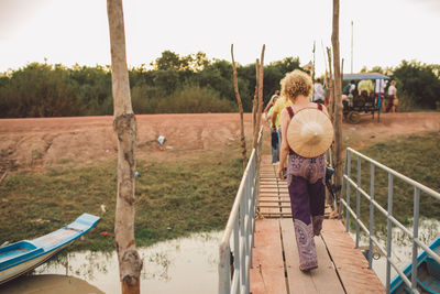 Rear view of woman walking on footbridge against sky