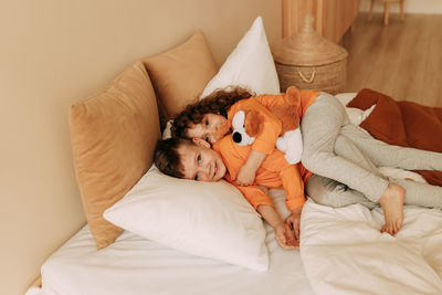 Funny happy kids brother and sister in pajamas playing having fun in a cozy bedroom at home